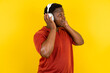 Young latin man wearing red t-shirt over yellow background wears stereo headphones listens music concentrated aside. People hobby lifestyle concept