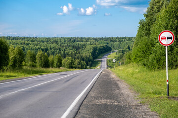 A road sign Overtaking is prohibited on a suburban highway through the forest on a sunny summer day. Beautiful landscape of nature and road.