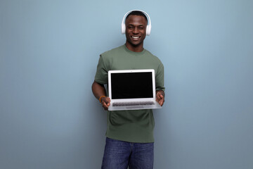 positive young smart american man in t-shirt shows laptop screen with mockup for web page. advertising concept