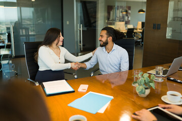 Wall Mural - Smiling pregnant businesswoman shaking hands with coworker in office conference room