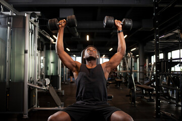 athletic african american man trains in dark gym, athletic guy lifts heavy dumbbells in fitness club