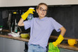 Portrait of  young tired tortured cleaning service woman. Housewife cleaner in yellow rubber gloves stands in the kitchen after a general cleaning of the house