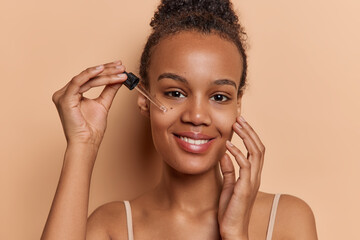 African girl has dark hair styled in bun immerses herself in transformative facial treatment applies essential oil to nurture radiant complexion involved in self pampering touches face gently