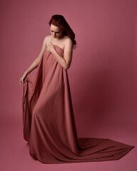 Poster - Portait of beautiful woman wearing gown of draped silk fabric, standing pose. Isolated on pink studio background.
