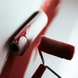 Close up of Roller painting a white wall with red paint