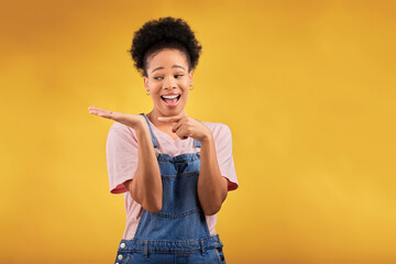 Wall Mural - Branding, advertising and a black woman pointing to her palm for the promotion of a product on a yellow background in studio. Smile, marketing or space with a happy young female brand ambassador