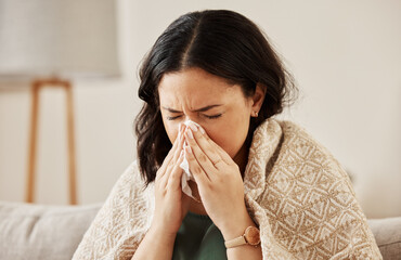 Nose, tissue and sick woman sneezing on a sofa with allergy, cold or flu in her home. Hay fever, allergy and female with viral infection, problem or health crisis in a living room with congestion