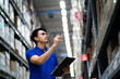 © KANGWANS - supply chain and logistic network technology concept. Happy Asian worker in blue uniform with clipboard in warehouse. Happy workers in the distribution center.