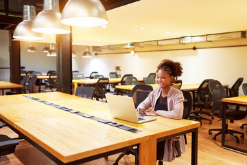 Wall Mural - portrait mid adult black woman sitting in office alone working with a laptop smiling