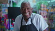 © Marco - Joyful African American senior staff of grocery store standing by cashier checkout wearing apron and smiling at camera, portrait close-up with friendly charismatic expression