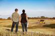 © Designpics - Farm couple standing in a field watching a combine finish their canola harvest, Alberta, Canada