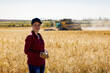 © Designpics - Portrait of a young farm woman standing in a mixed crop grain field at harvest time, while a combine works in the background; Alcomdale, Alberta, Canada