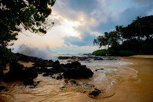 Secret Beach With View Through Silhouetted Palm Trees And Lava Rocks With Ocean Surf Breaking On The Shore At Makena Cove; Maui, Hawaii, United States Of America