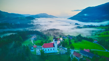 Wall Mural - Aerial drone view of small beautiful church on valley in Slovenia at dawn. Beautiful summer morning landscape..