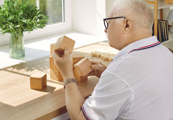 Wall Mural - Demented senior patient playing brain game. Old man with Alzheimer's disease looking at wooden cube that he's holding in hand while sitting at desk in geriatric clinic or nursing home Dementia concept