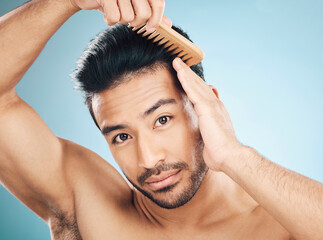 Poster - Portrait, beauty and a man brushing his hair on a blue background in studio for self grooming. Face, morning and routine with a young male model in the bathroom for style after shampoo treatment