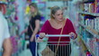 © Marco - Female Customer pushing shopping cart at grocery store isle. woman in 50s picking products from shelf