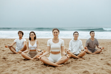 Wall Mural - Youngsters finding balance with beach yoga, meditating in lotus position, enjoying morning training on ocean shore