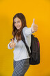 little cute schoolgirl with backpack over her shoulders keeps her fingers up in gesture up