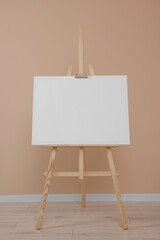 Wall Mural - Wooden easel with blank canvas near beige wall indoors