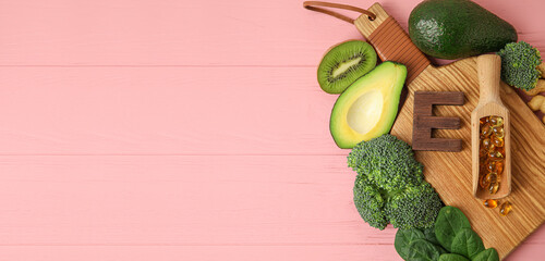 Board with healthy products rich in vitamin E and pills on pink wooden background with space for text