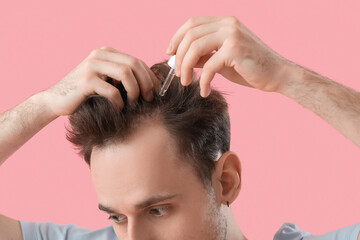Wall Mural - Young man using serum for hair growth on pink background, closeup