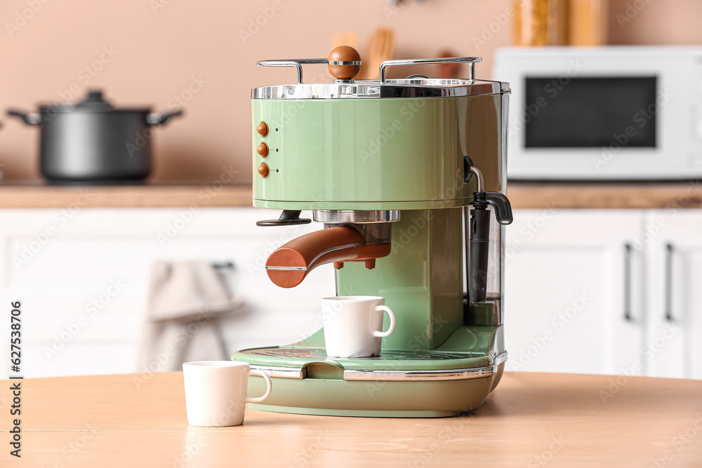 Modern coffee machine with cups on wooden table in kitchen