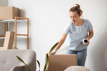 Wall Mural - Young woman wrapping cardboard box with stretch film at home