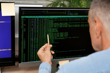 Wall Mural - Male programmer pointing at computer monitor with command line interface, closeup