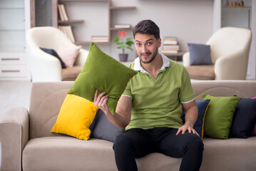 Wall Mural - Young man with a lot of pillows sitting on the sofa