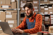 © Andrii Lysenko - Focused warehouse employee working on laptop in a large storehouse sitting at the table