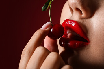 Wall Mural - Beautiful woman with red lips and cherry on dark background, closeup