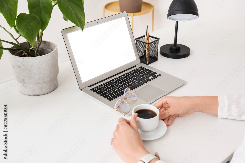 Female hands with cup of coffee and laptop at white table