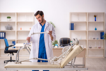 Wall Mural - Young male doctor with skeleton in the clinic