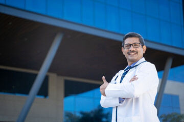 Poster - Indian doctor standing in front of hospital and showing thumps up