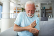 An elderly man experiences discomfort and pain in his fingers and hands. Old man with finger pain, showcasing his actions of massaging his arthritic hand and wrist