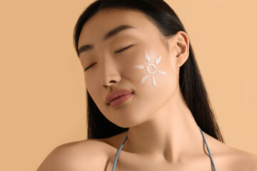 Poster - Beautiful young woman with sun protection cream on her face against beige background