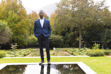 Wall Mural - Thoughtful african american groom standing by pond in sunny garden, copy space