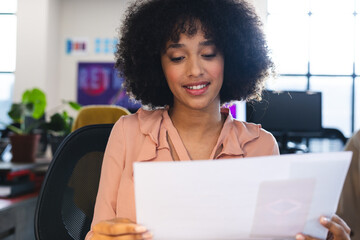 Fototapete - Biracial woman reading a document during a video call at office
