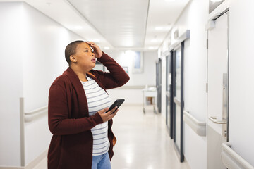 Wall Mural - Worried african american female patient using smartphone in waiting room at hospital, copy space