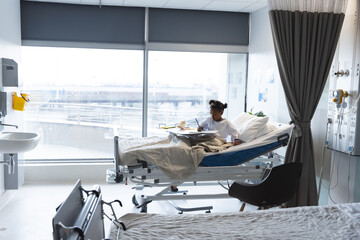 Wall Mural - African american girl patient lying on bed colouring in patient room at hospital, copy space