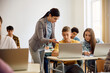 © Drazen - High school teacher assists her students in using laptop during computer class.