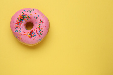 Tasty glazed donut decorated with sprinkles on yellow background, top view. Space for text