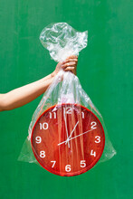 Crop Person Holding Plastic Bag With Red Clock In Studio