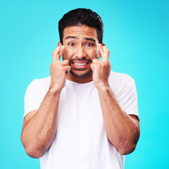 Leinwandbilder - Fear, hope and portrait of man fingers crossed, anxiety or nervous due to crisis or stress isolated in studio blue background. Worry, suspense and young male person hands in face for mistake reaction