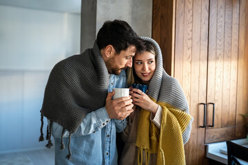 Canvas Print - Happy young couple with hot drinks cuddling under warm blanket at home