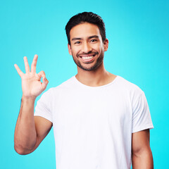 Poster - Happy, perfect gesture and portrait of a man in a studio with an agreement sign or expression. Happiness, smile and young Indian male model with an approval hand emoji isolated by a blue background.