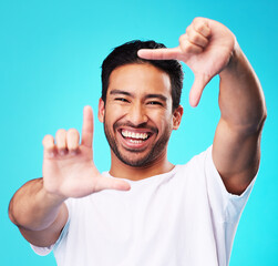 Poster - Happy, hand frame and portrait of a man for a selfie, creative aesthetic or advertising photography. Smile, laughing and face of an Asian person with a gesture for a photo on a blue background