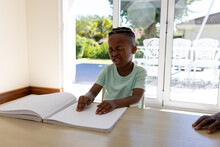 Sight Impaired African American Boy Reading Braille Book At Home In Sunny Living Room