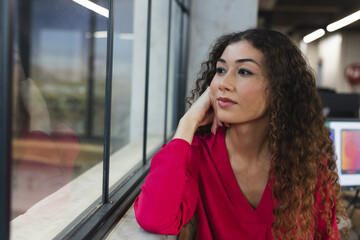 Thoughtful biracial woman looking out of the window at office
